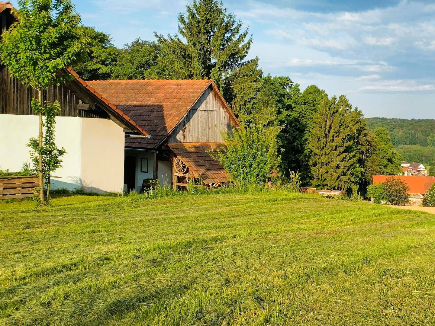 Idyllisches Landhaus mit rotem Ziegeldach und Holzverkleidung, eingebettet in eine grüne Hügellandschaft.