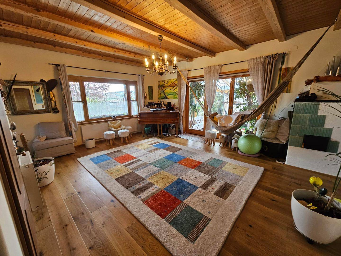 Gemütliches Wohnzimmer mit Holzbalkendecke, Parkettboden und einem bunten Teppich.