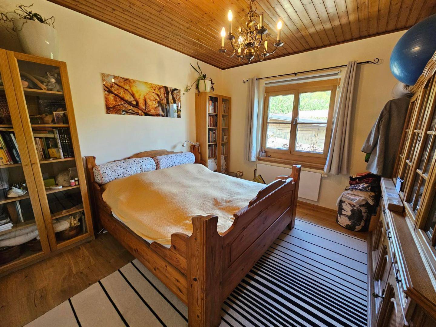Schlafzimmer mit Holzbett, Holzbalkendecke und einem Fenster mit Blick ins Grüne.