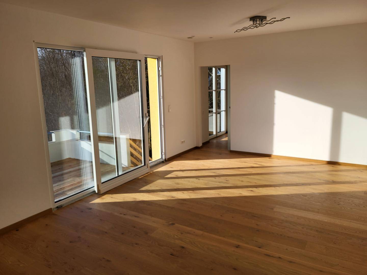 Lichtdurchfluteter Wohnbereich mit Holzboden und Zugang zur Außenterrasse.