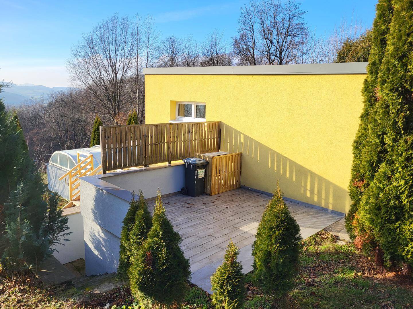 Kleine gepflasterte Terrasse neben dem Haus mit Sichtschutz und Blick ins Grüne.