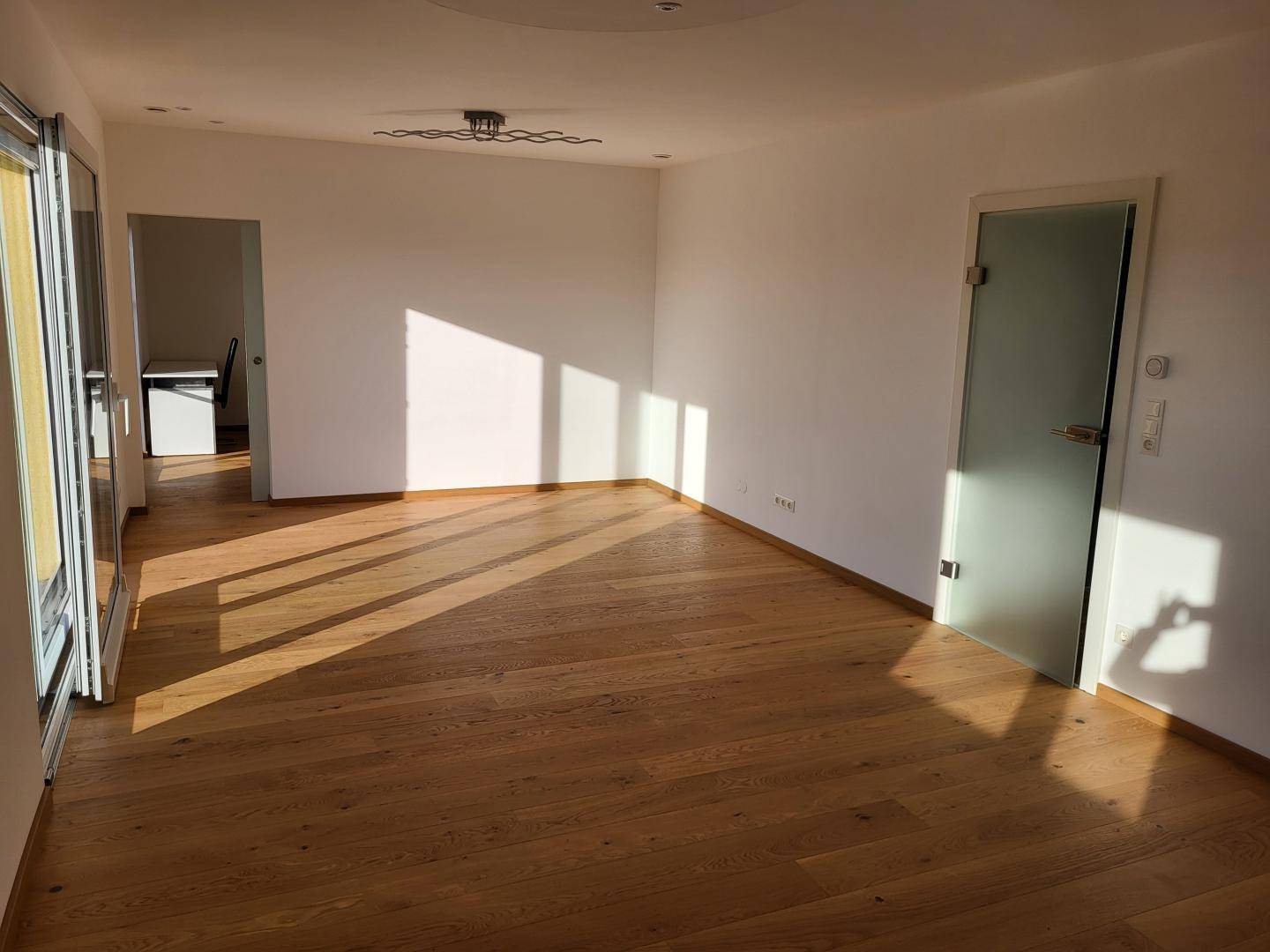 Helles Wohnzimmer mit Eichenparkettboden und viel natürlichem Licht durch große Fenster.