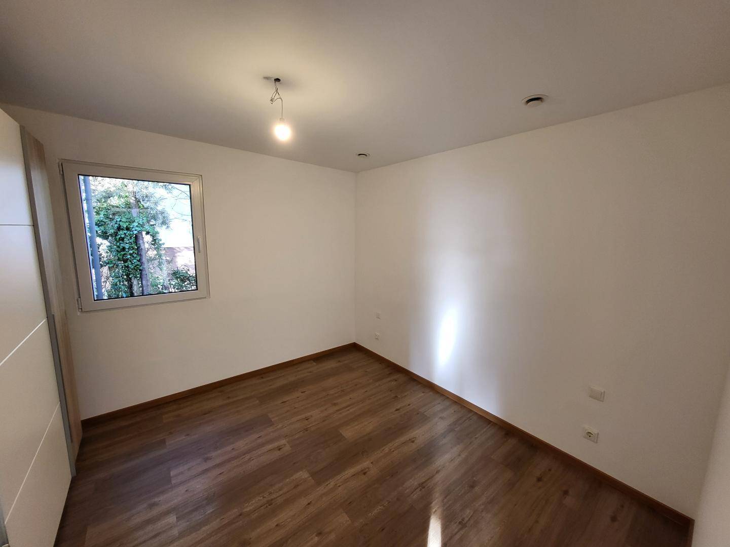 Kleines Schlafzimmer mit Laminatboden und einem Fenster mit Blick ins Grüne.