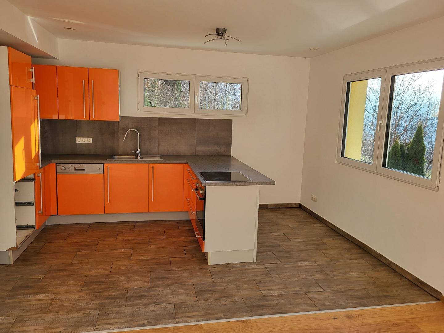 Moderne Küche mit leuchtend orangefarbenen Fronten, integrierten Geräten und Essbereich.