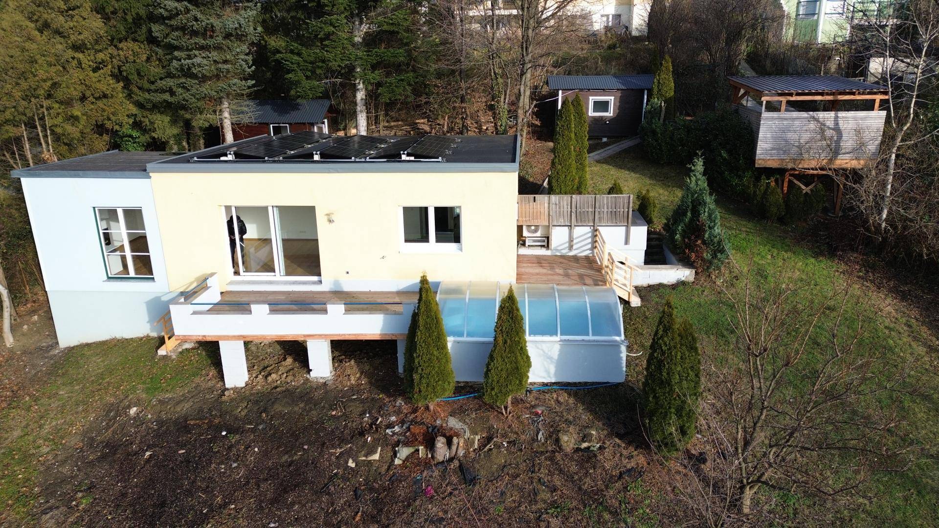 Gesamtansicht des modernen Hauses mit Photovoltaikanlage auf dem Flachdach und umgebender Natur.