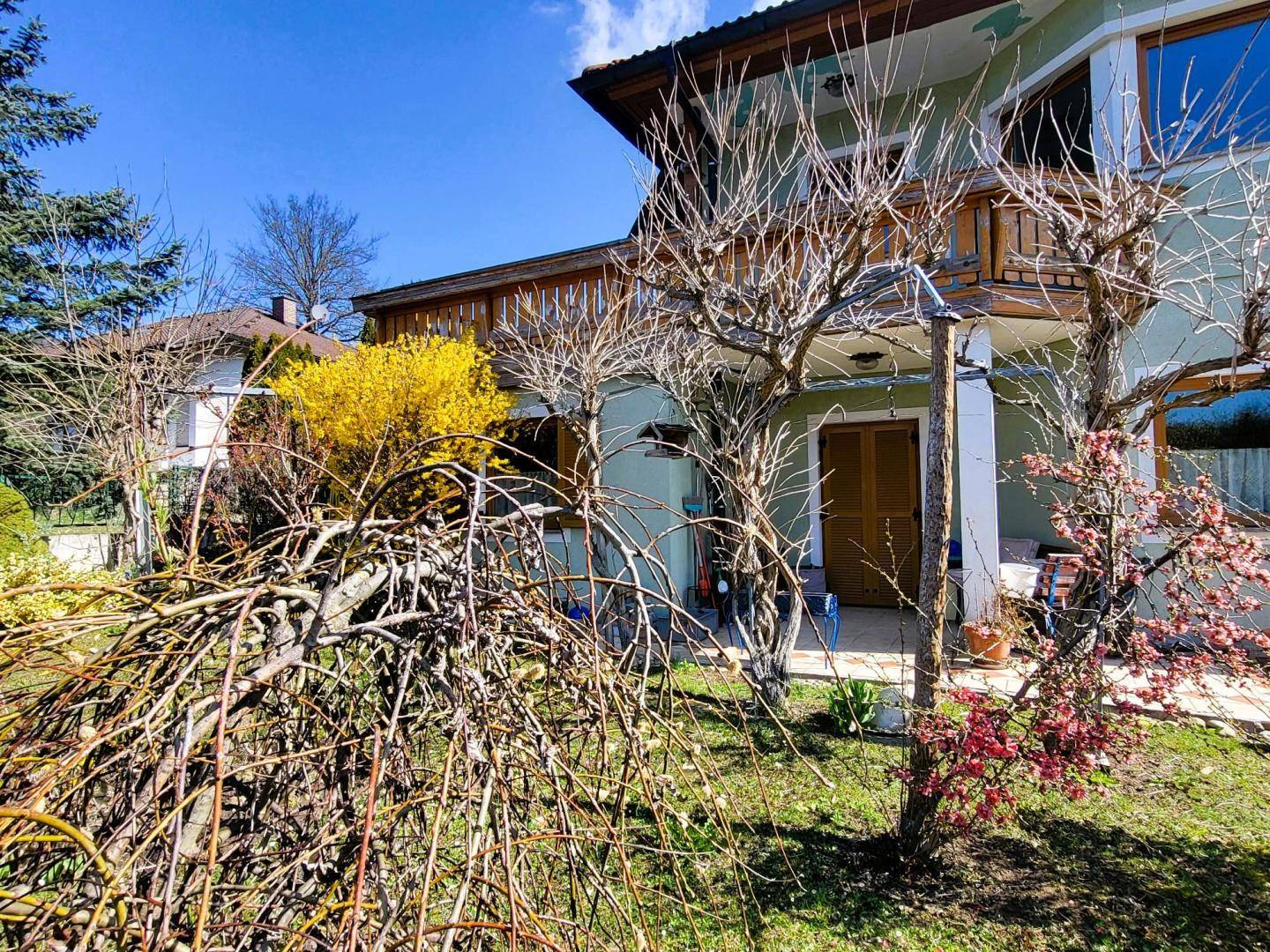 Ansicht des Hauses mit hellgrüner Fassade und einem blühenden Garten im Vordergrund unter blauem Himmel.