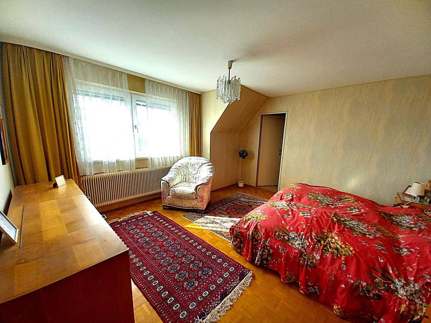 Schlafzimmer mit Doppelbett, Kommode, Fenster und einem roten Teppich, dekoriert mit gelben Vorhängen.