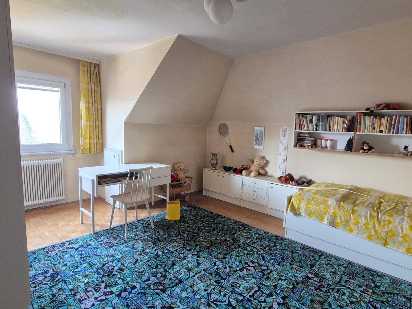 Kinderzimmer mit Dachschräge, Einzelbett, Schreibtisch und Bücherregal, dekoriert mit gelben Akzenten.