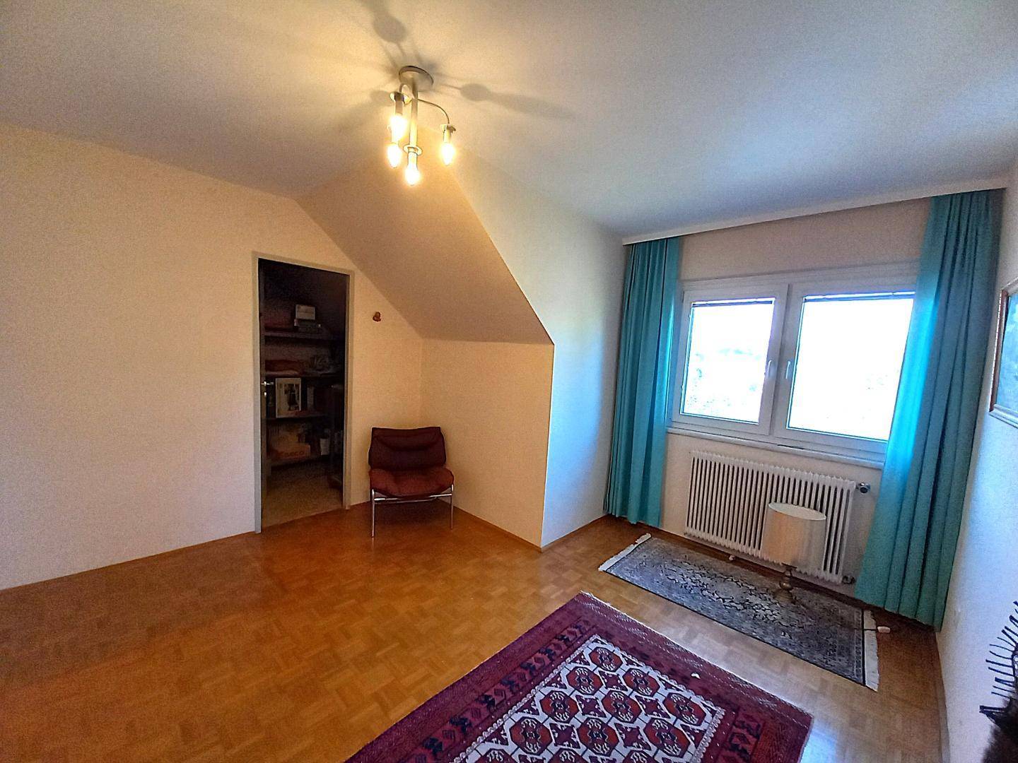 Leeres Schlafzimmer mit Dachschräge, Fenster und einem begehbaren Schrank oder Abstellraum.
