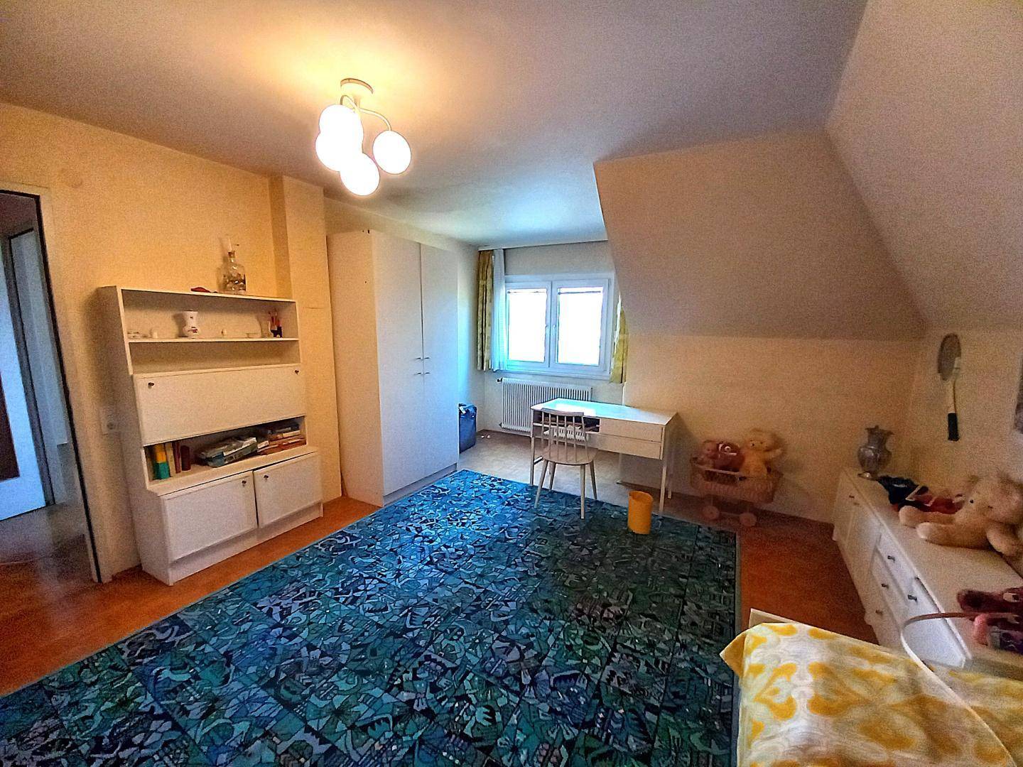 Weiterer Blick ins Kinderzimmer mit Dachschräge, Fenster und praktischen Aufbewahrungsmöbeln.