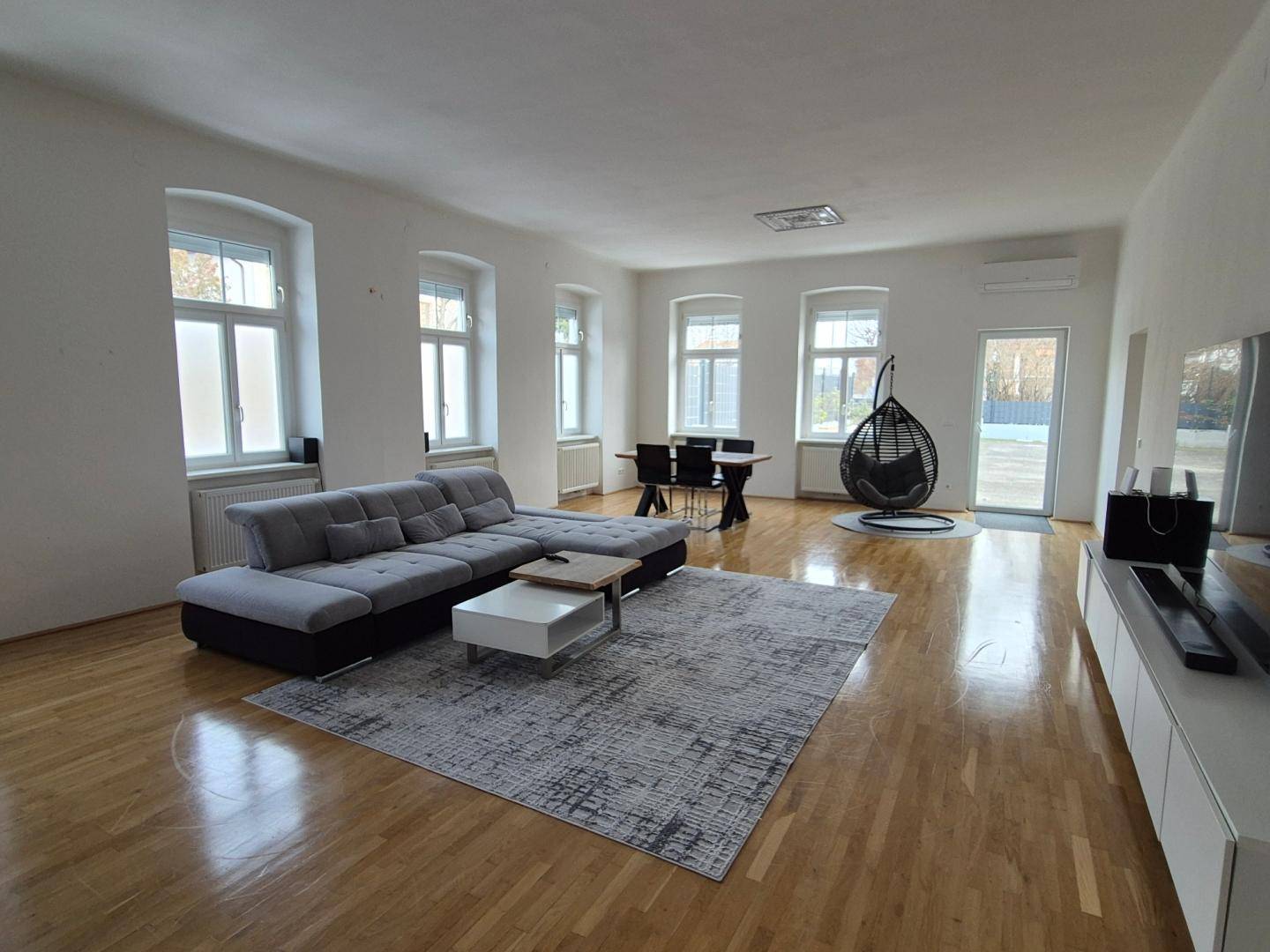 Geräumiger offener Wohn- und Essbereich mit Holzboden, großem Sofa und Hängesessel.