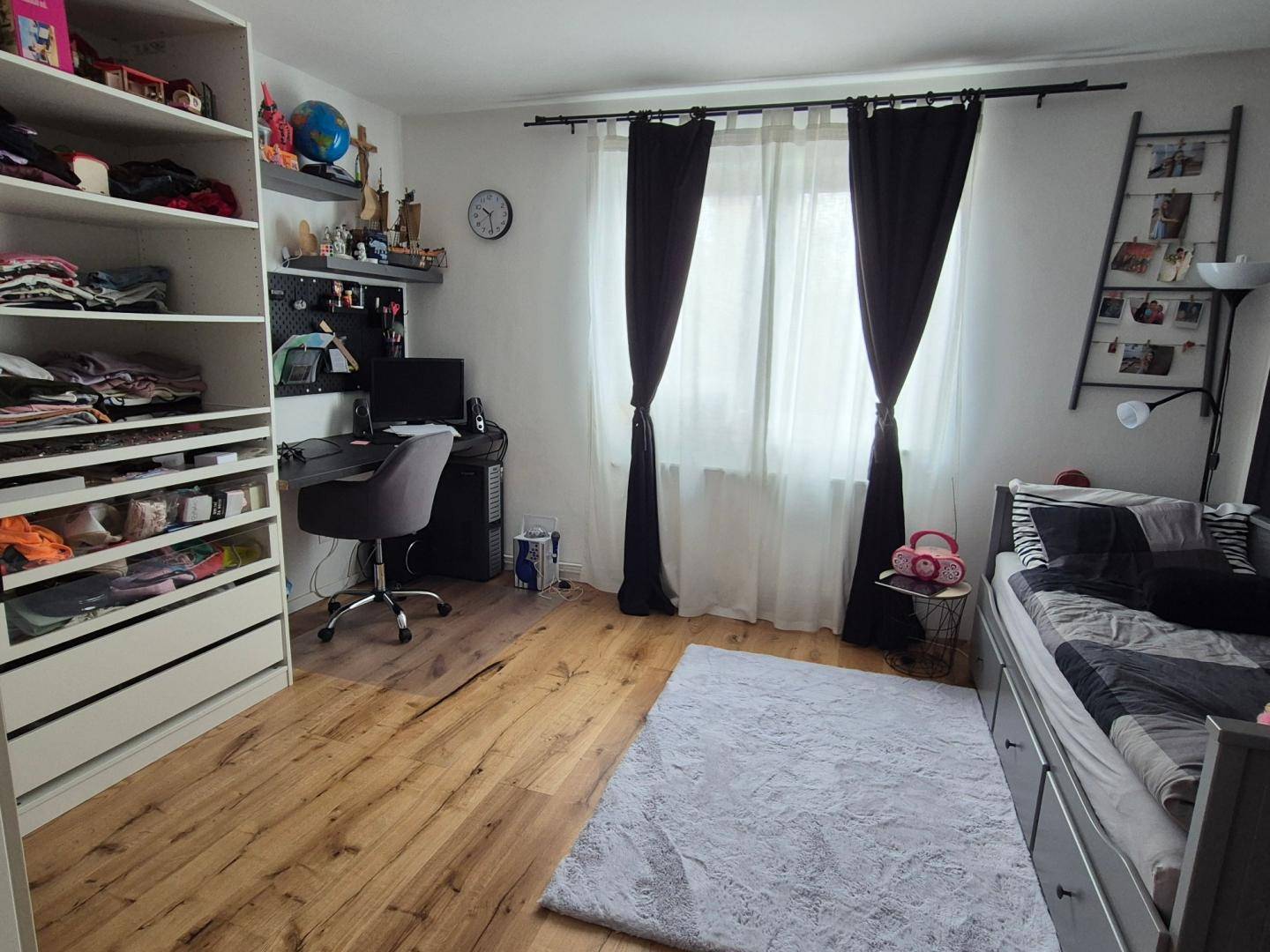 Kinder- oder Arbeitszimmer mit Holzboden, Schreibtisch und großem Fenster.