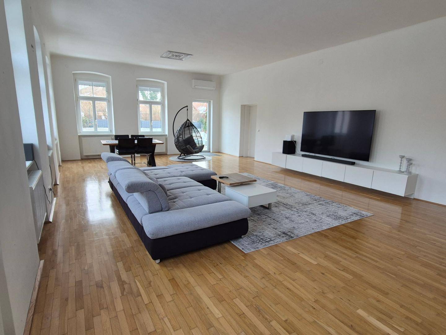 Heller Wohnbereich mit Holzboden, großem Fernseher und modernem Sofa.