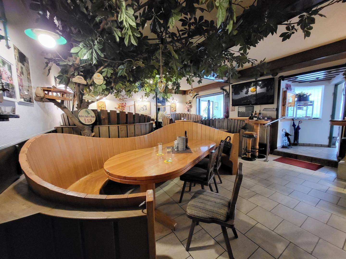 Gemütlicher Restaurantbereich mit rustikalen Holzbänken, einem großen Holztisch und künstlicher Begrünung an der Decke.