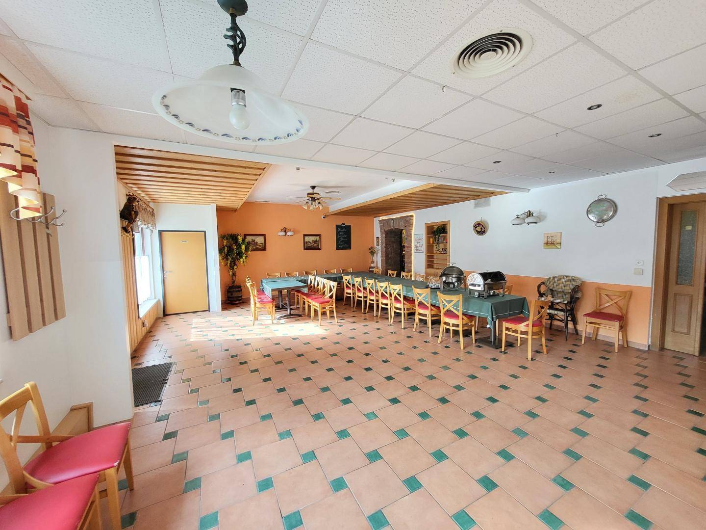Großer Speisesaal mit vielen Tischen und Stühlen, Fliesenboden und einer hellen Farbgestaltung.