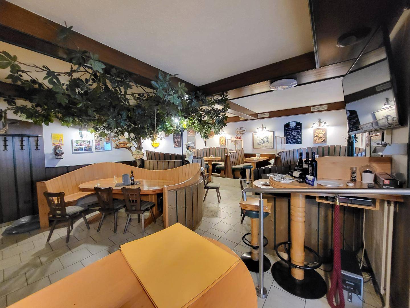 Weiterer Restaurantbereich mit geschwungenen Holzbänken, dunklen Holzbalken und einem kleinen Barbereich.