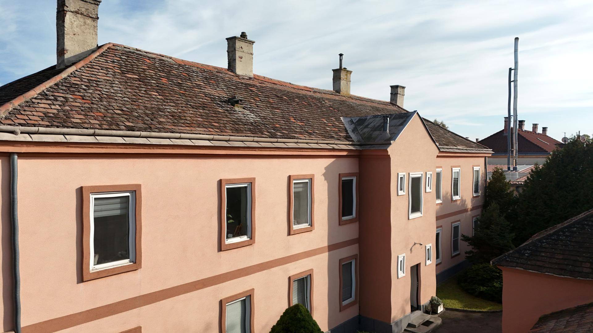 Seitenansicht des Gebäudes mit rosafarbener Fassade, weißen Fensterrahmen und Ziegeldach.