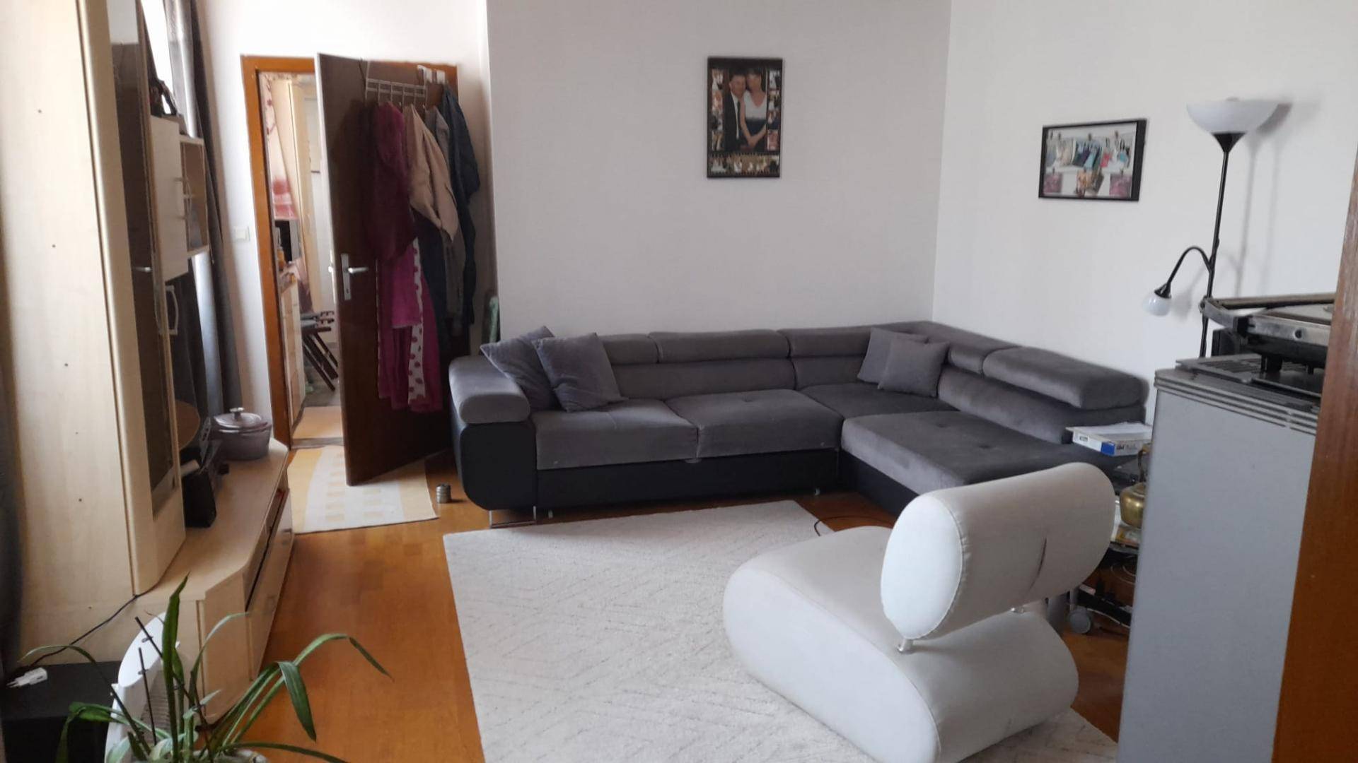 Helles Wohnzimmer mit großem grauen Ecksofa, weißem Sessel und Holzboden.