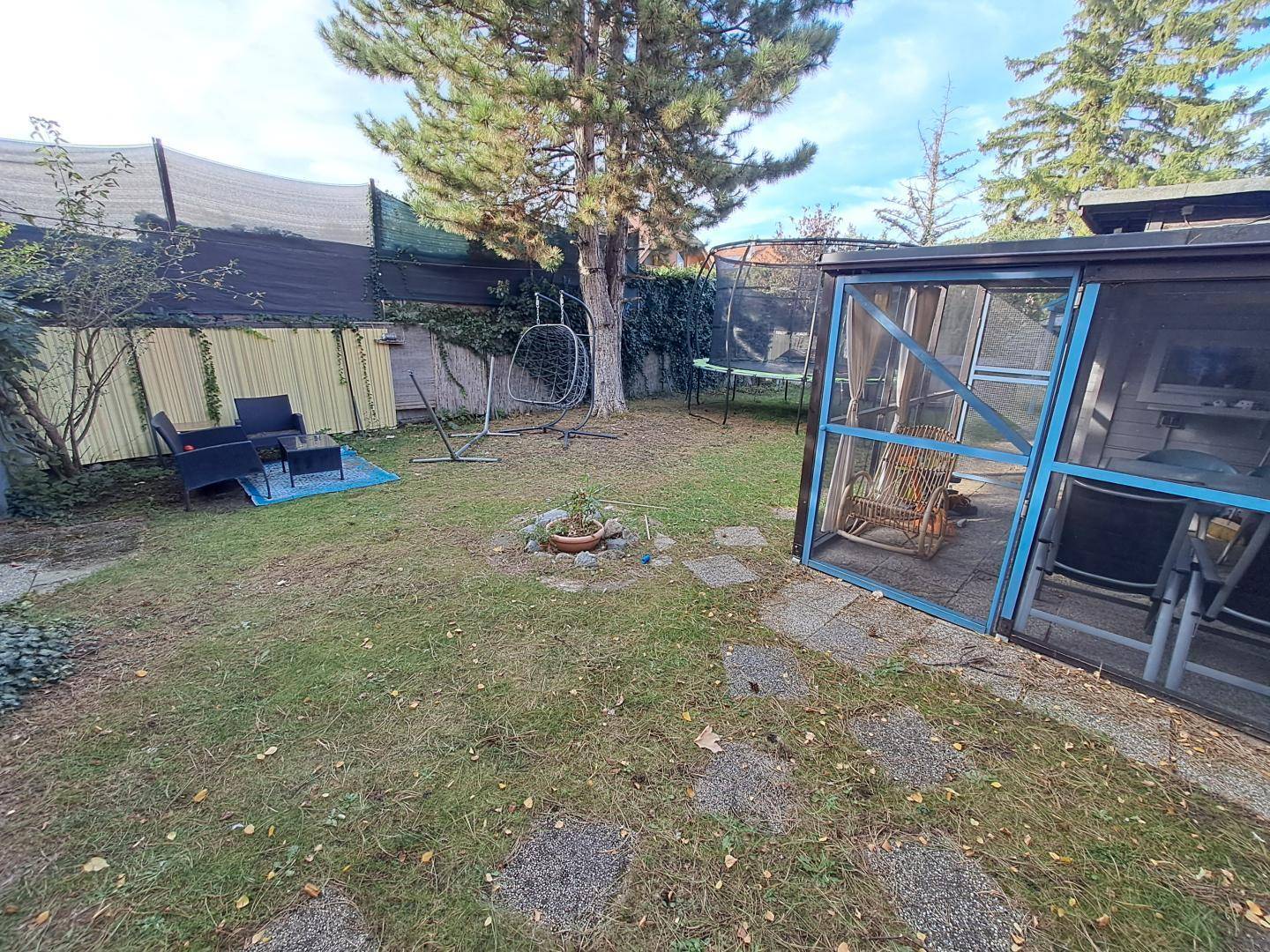 Gepflegter Garten mit Rasenfläche, Outdoor-Sitzgelegenheiten und einem kleinen Gewächshaus oder Pavillon.