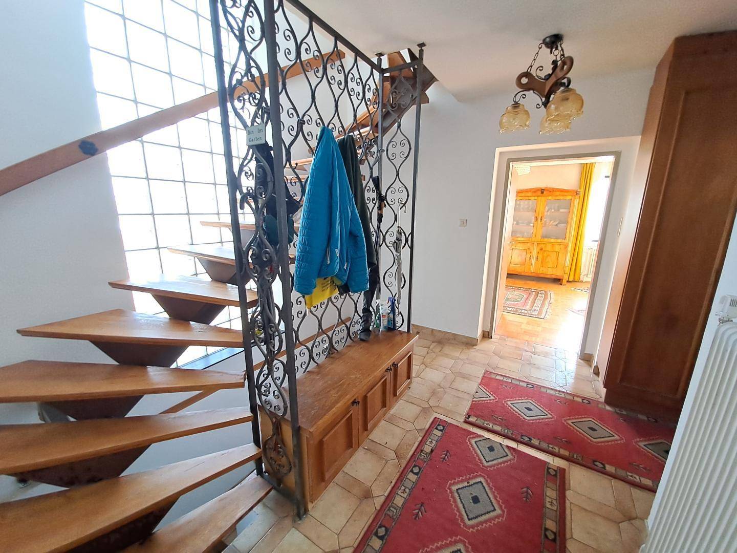 Heller Eingangsbereich mit offener Holztreppe und schmiedeeisernem Geländer.
