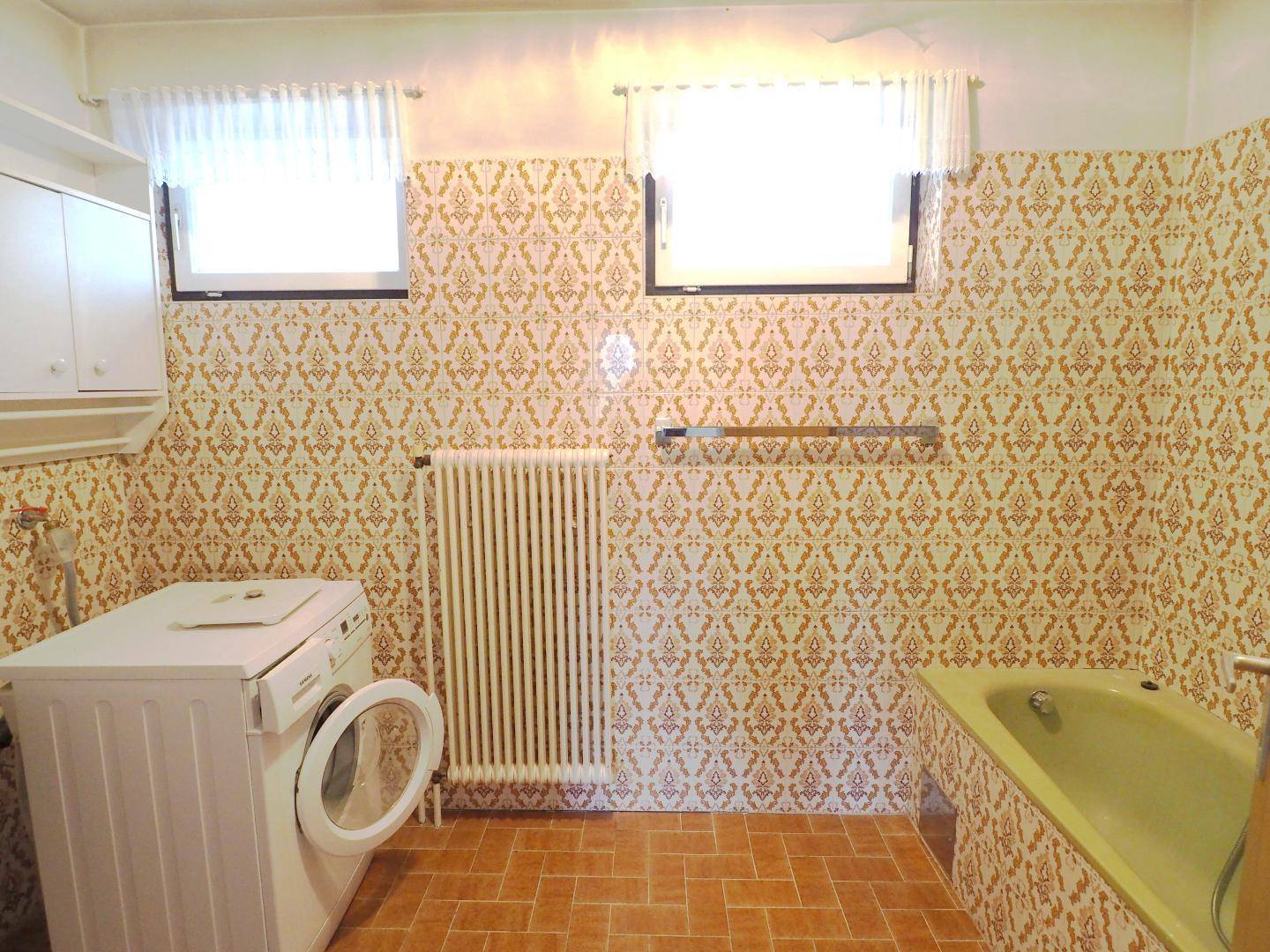 Badezimmer mit gemusterten Fliesen, Badewanne und Fenster für Tageslicht.
