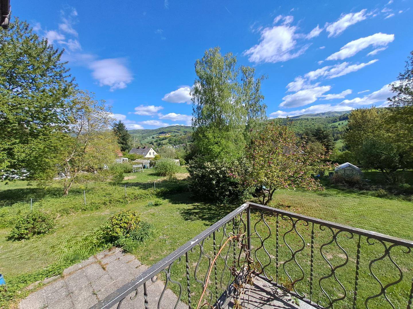 Balkon mit schmiedeeisernem Geländer und Panoramablick auf die grüne Umgebung und Berge.