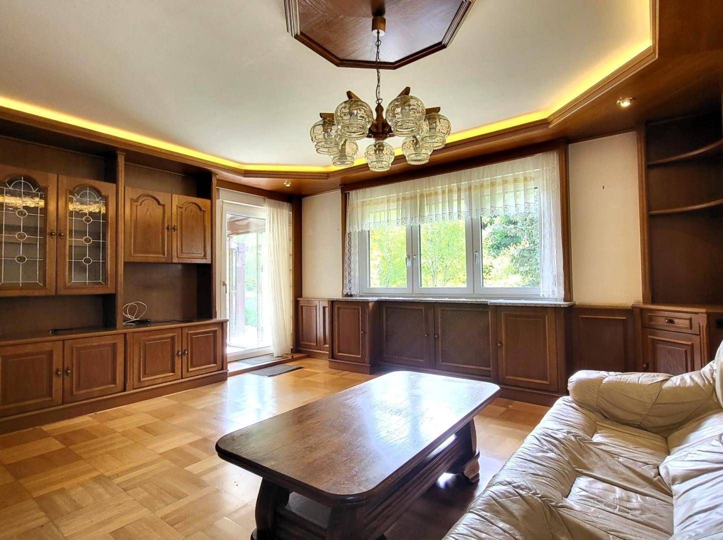 Geräumiges Wohnzimmer mit Parkettboden, Holzvertäfelung und großem Fenster zum Garten.