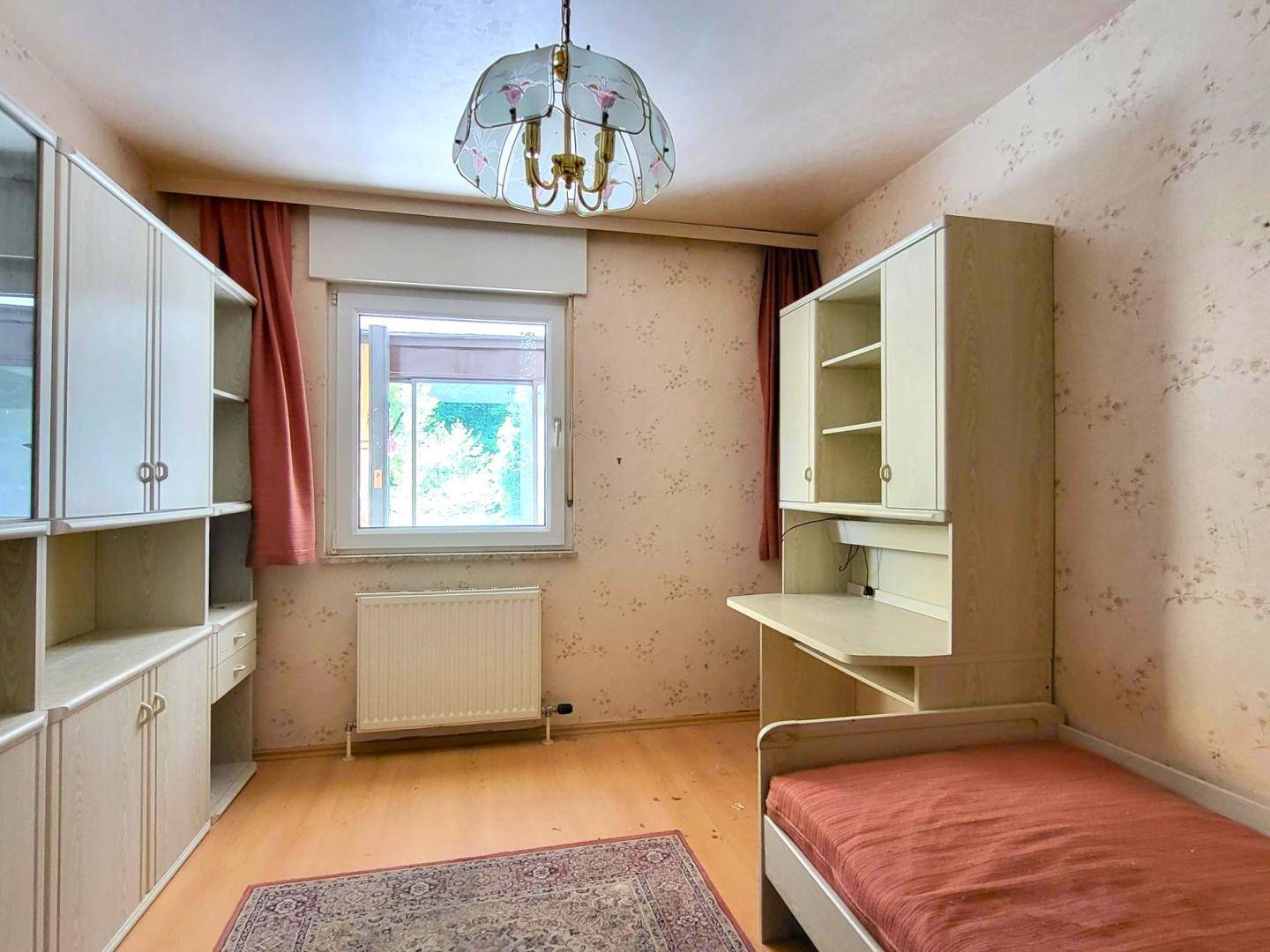 Schlafzimmer mit Einzelbett, Schreibtisch, Einbauschränken und Fenster.