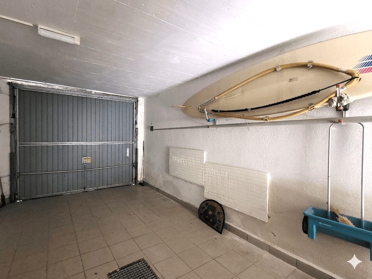 Funktionale Garage mit Fliesenboden, geschlossenem Tor und praktischem Stauraum an der Wand.