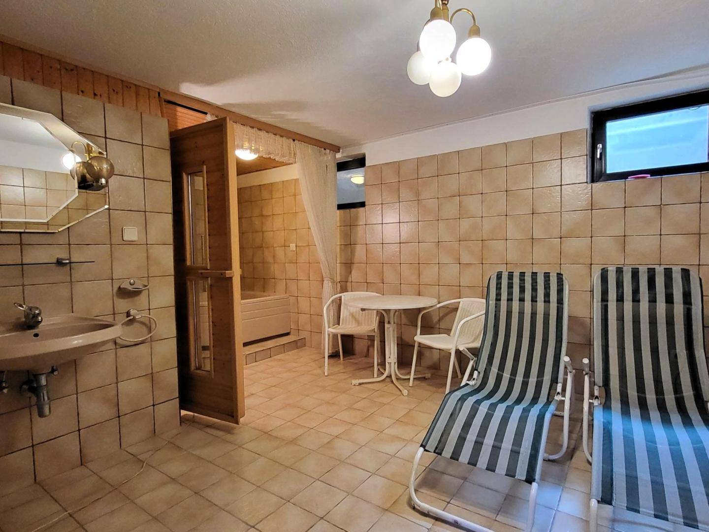 Gefliester Wellnessbereich mit Liegestühlen, Waschbecken und Zugang zu einer Sauna.