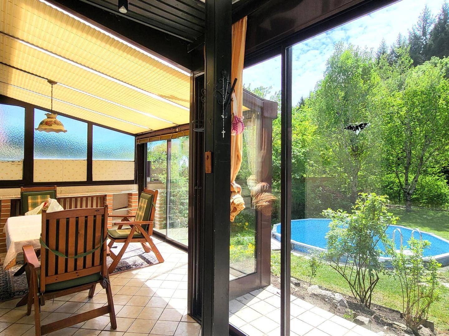 Heller Wintergarten mit Essbereich, Fliesenboden und weitem Blick auf den Garten und Pool.
