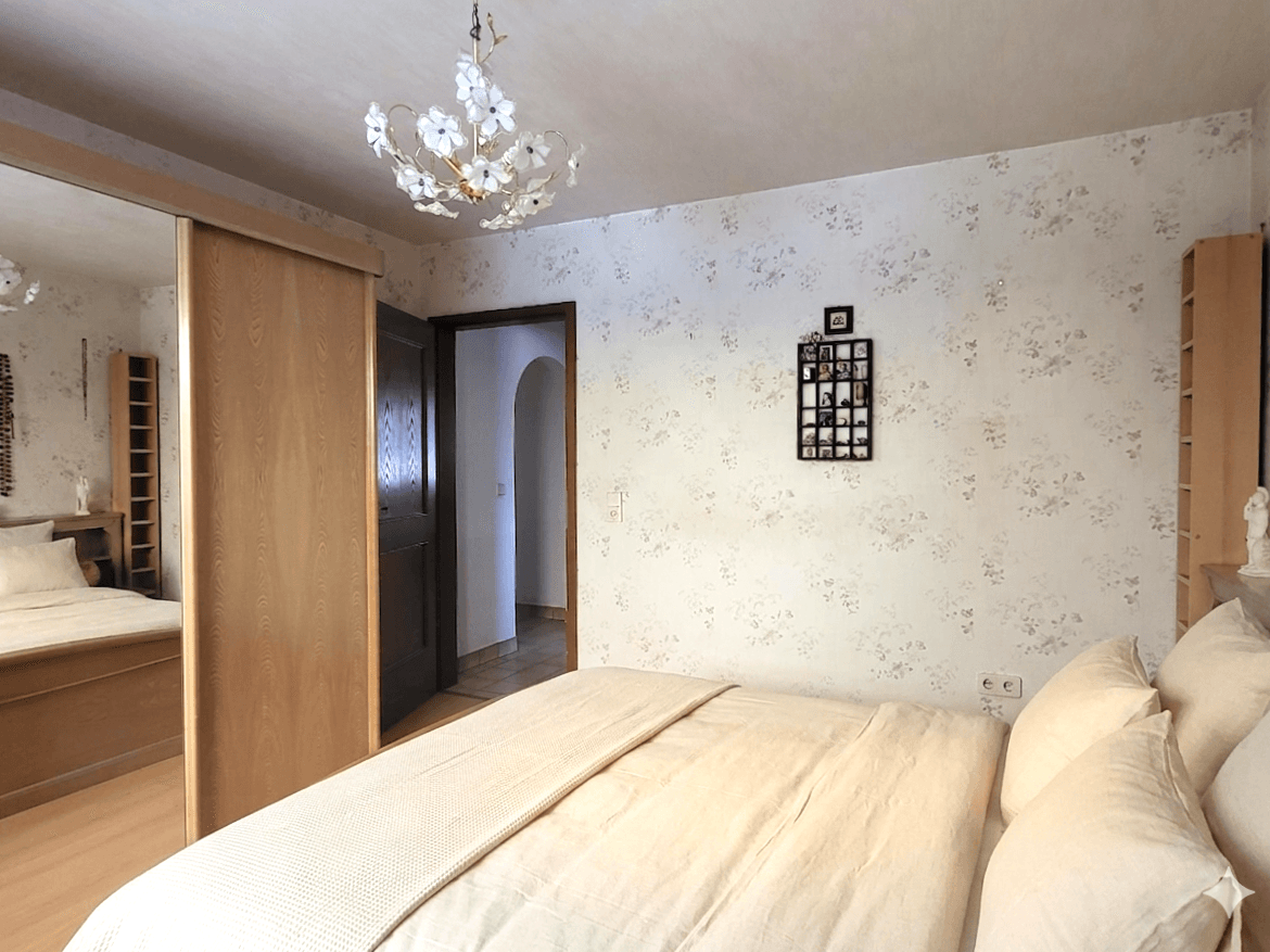 Gemütliches Schlafzimmer mit floraler Tapete, großem Bett und praktischem Spiegelschrank.