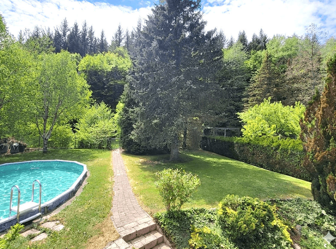 Großer Garten mit ovalem Aufstellpool und weitem Blick auf die umliegende Waldlandschaft.