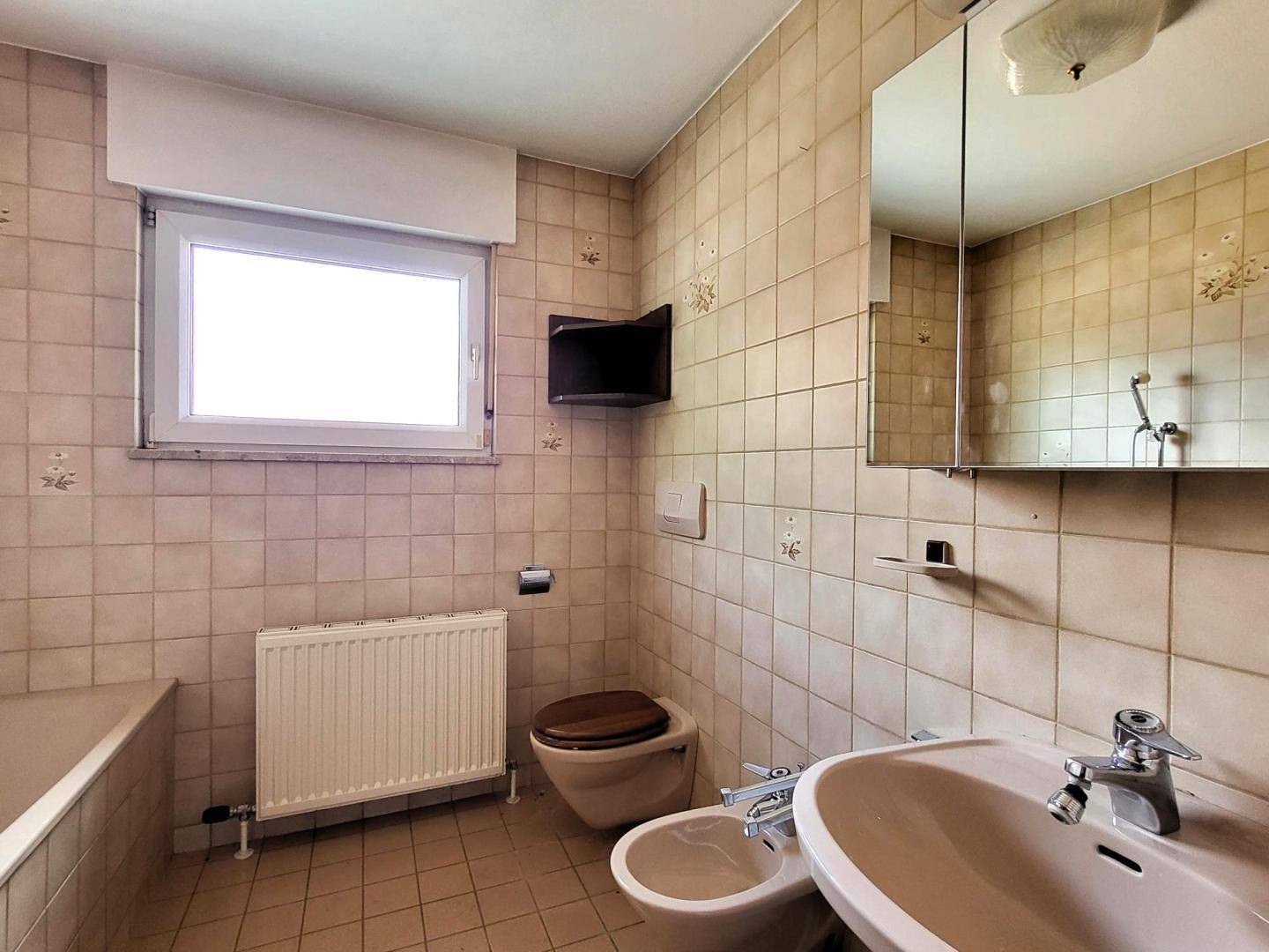 Badezimmer mit beigefarbenen Fliesen, Fenster, Badewanne, WC und Bidet.
