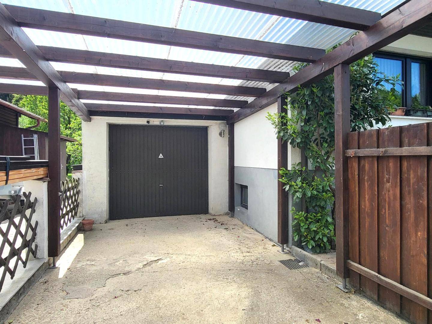 Geräumiger Carport mit Wellblechdach und geschlossener Garage, umgeben von Grün.