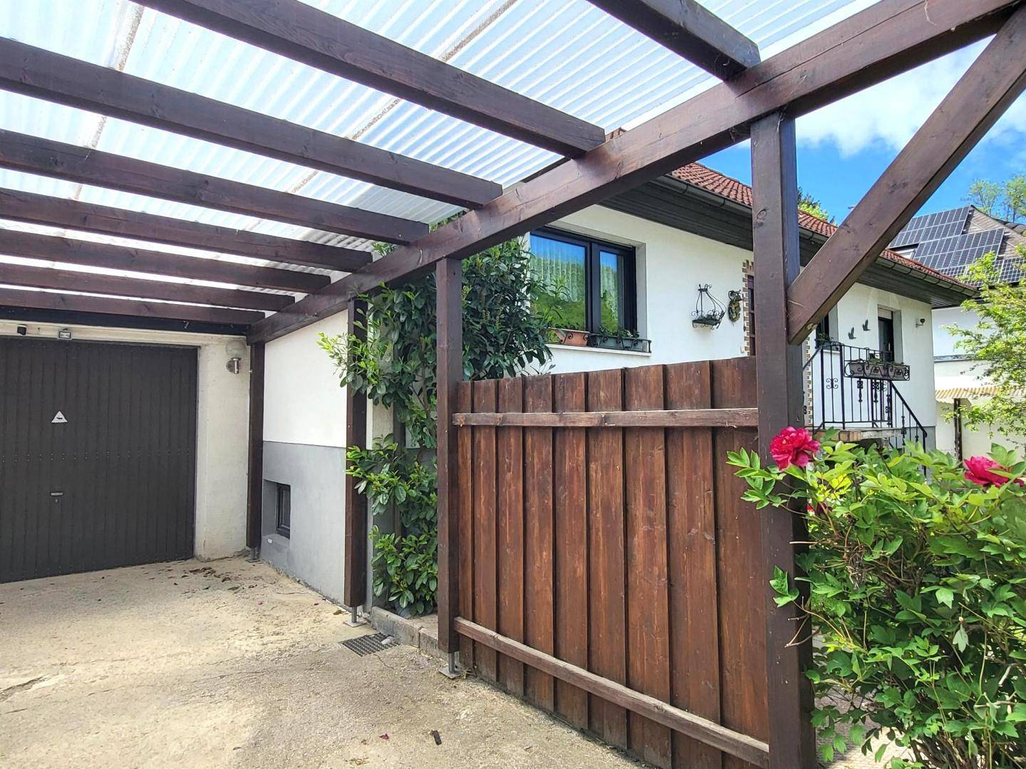 Überdachter Carport-Bereich mit direktem Zugang zur Garage und Holzzaun.