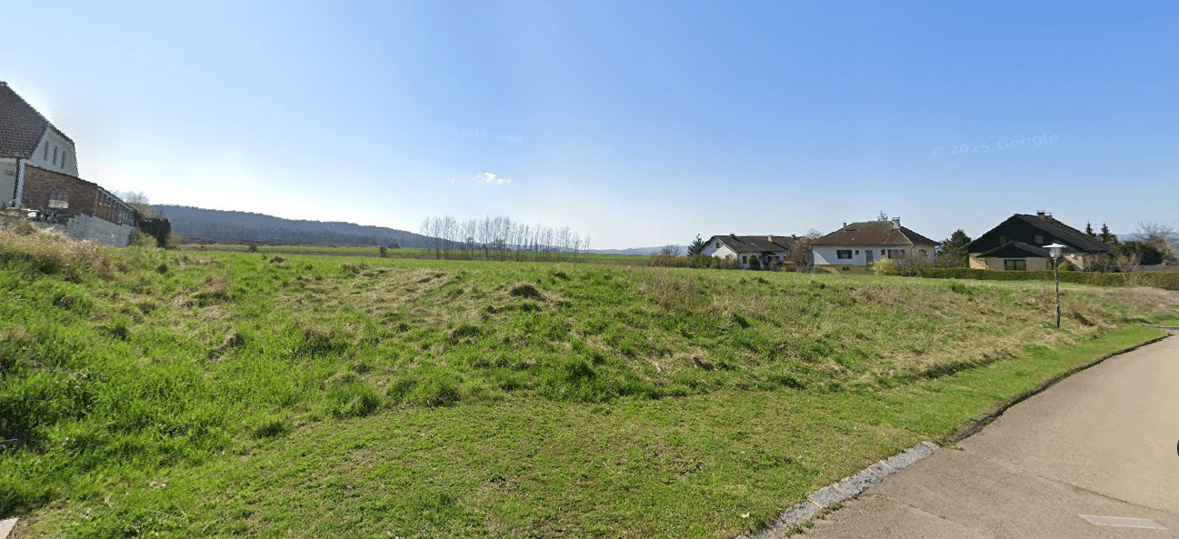 Grundstück an einer ruhigen Straße mit Blick auf umliegende Häuser und die weite Landschaft.