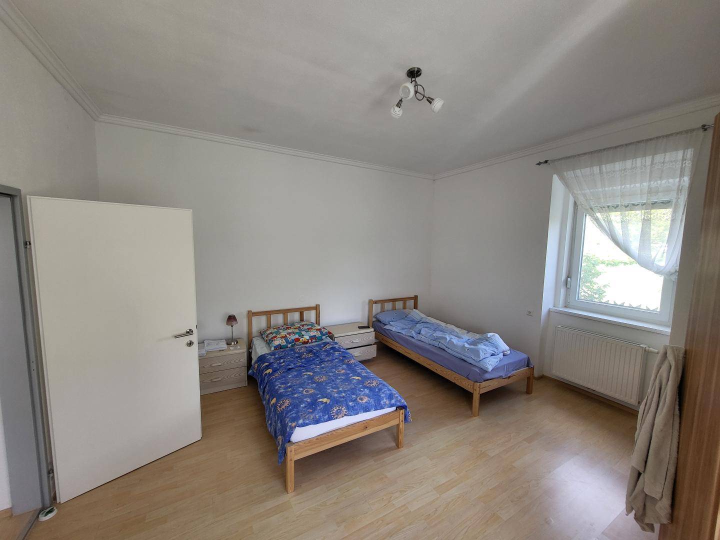 Helles Schlafzimmer mit zwei Einzelbetten, Laminatboden und Fenster.