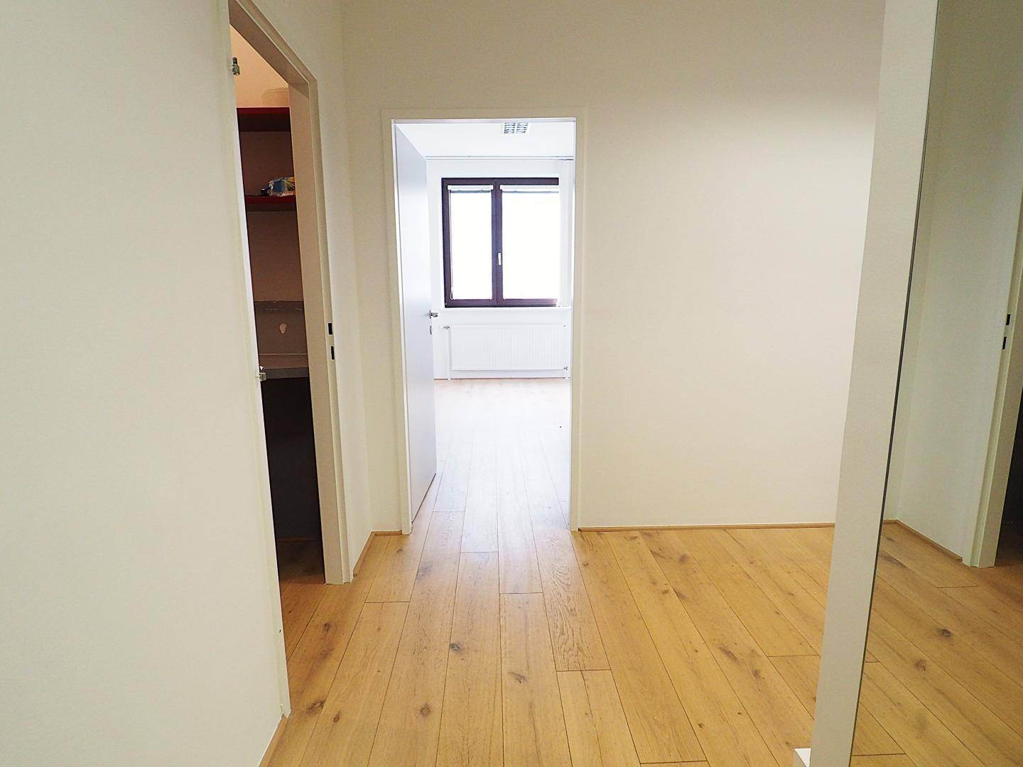 Heller Flur mit Holzboden, weißen Wänden und Durchgängen zu weiteren Zimmern der Wohnung.