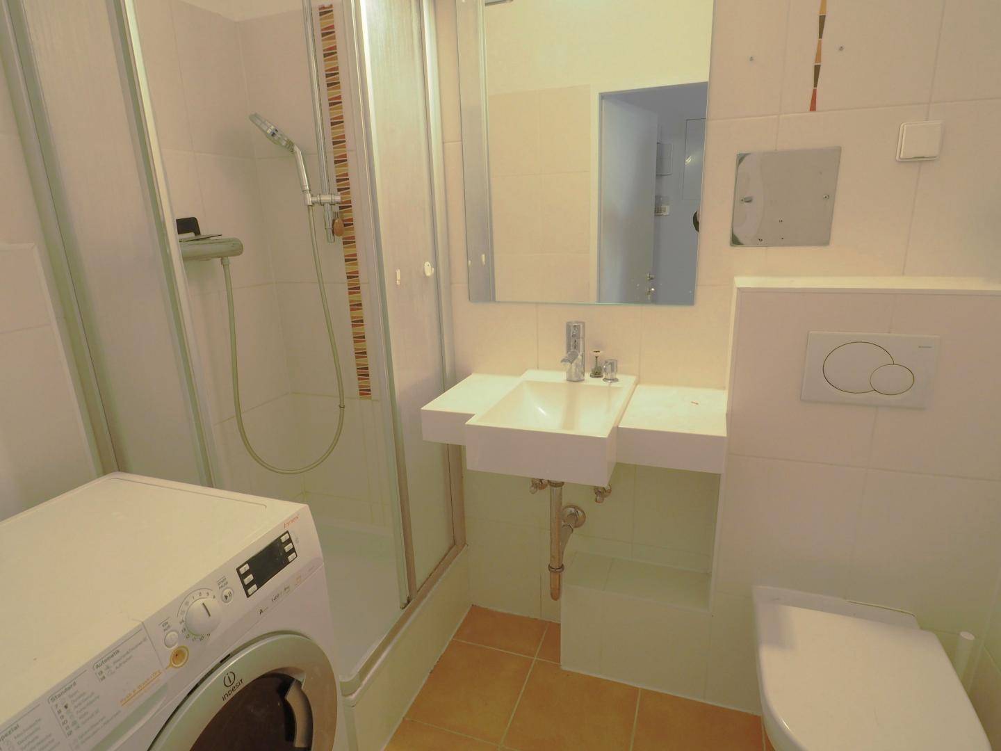 Funktionales Badezimmer mit Duschkabine, Waschbecken, Toilette und integrierter Waschmaschine.