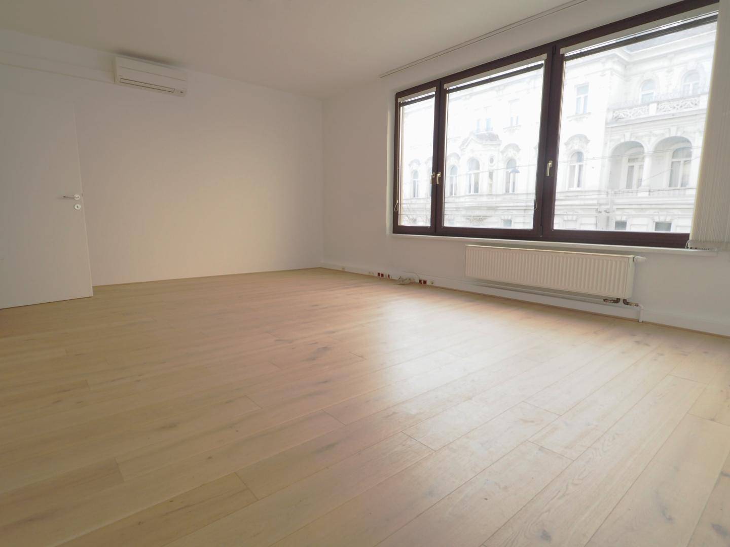 Heller Wohnraum mit neuem Holzboden, großen Fenstern und Blick auf ein historisches Gebäude.
