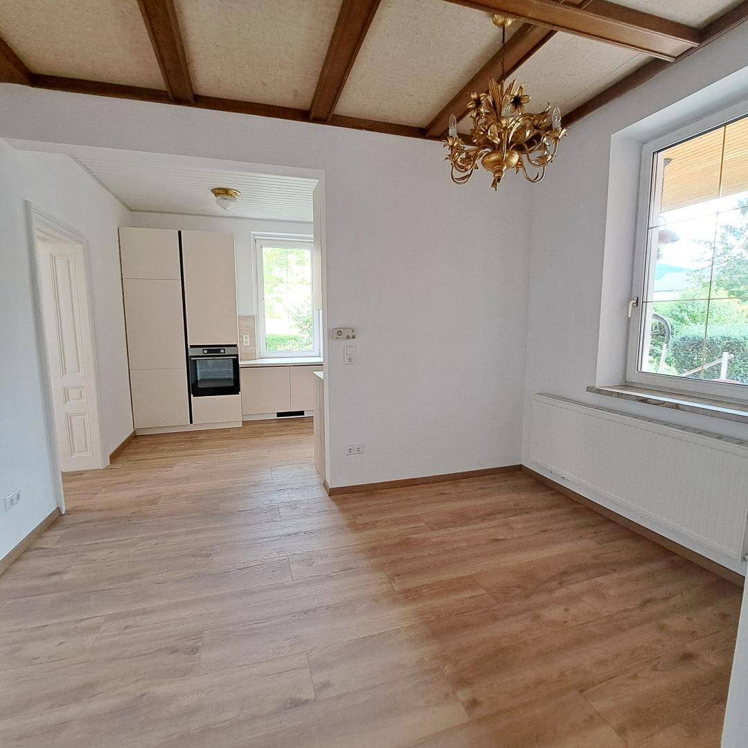 Wohnbereich mit Holzbalkendecke und offenem Übergang zur modernen Küche.