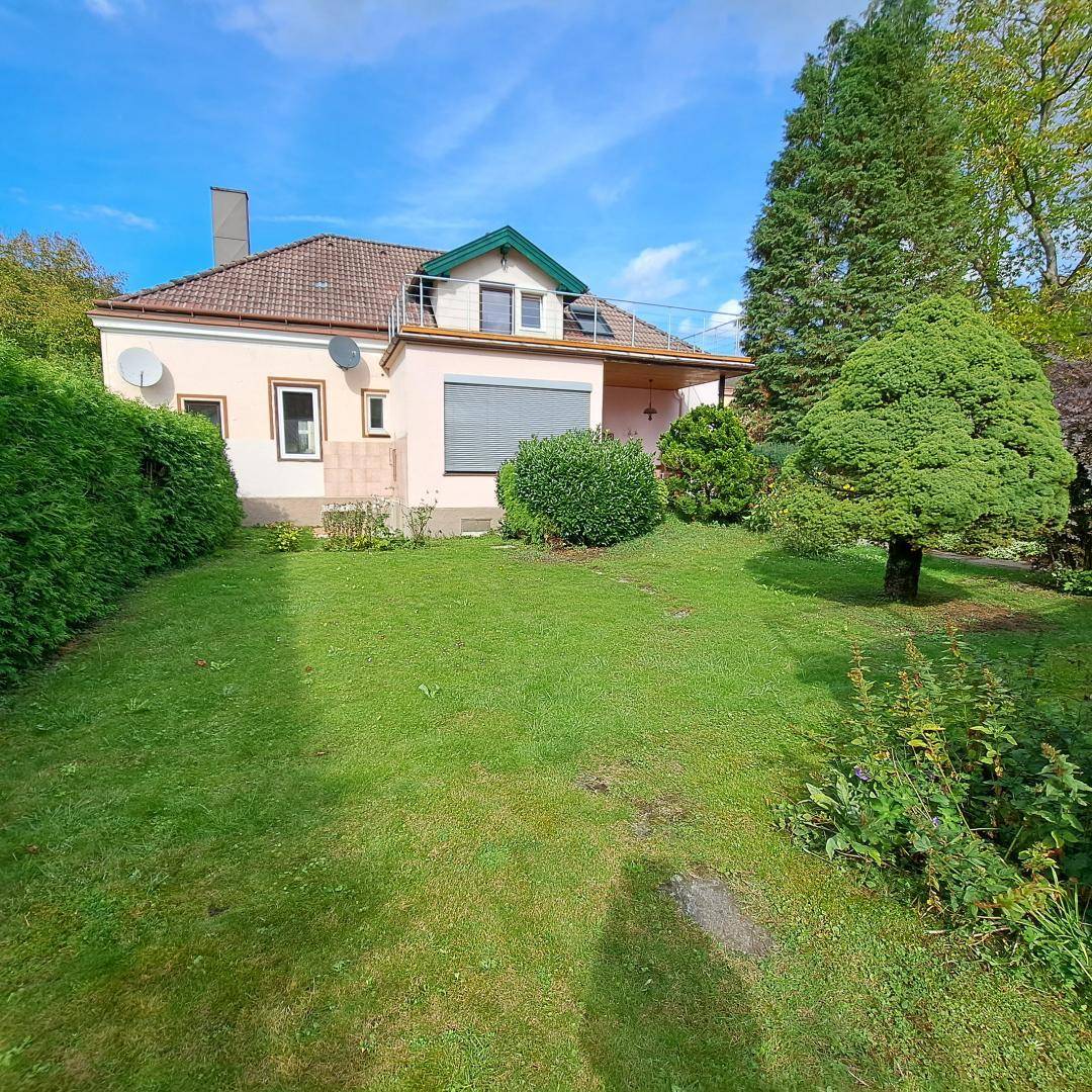 Gepflegter Garten mit großer Rasenfläche, hohen Hecken und dem Haus im Hintergrund.