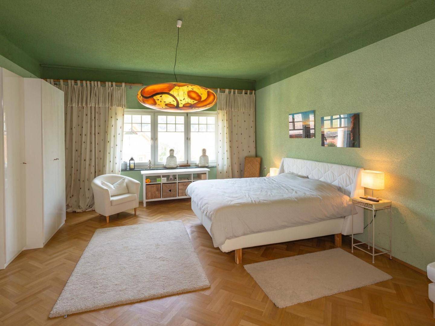 Helles Schlafzimmer mit grünen Wänden, Parkettboden und einem großen Fenster.