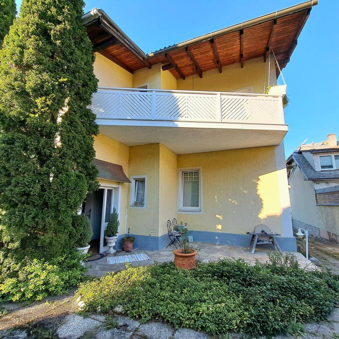 Gelbe Hausfassade mit Balkon, kleiner Terrasse und gepflegtem Vorgartenbereich.