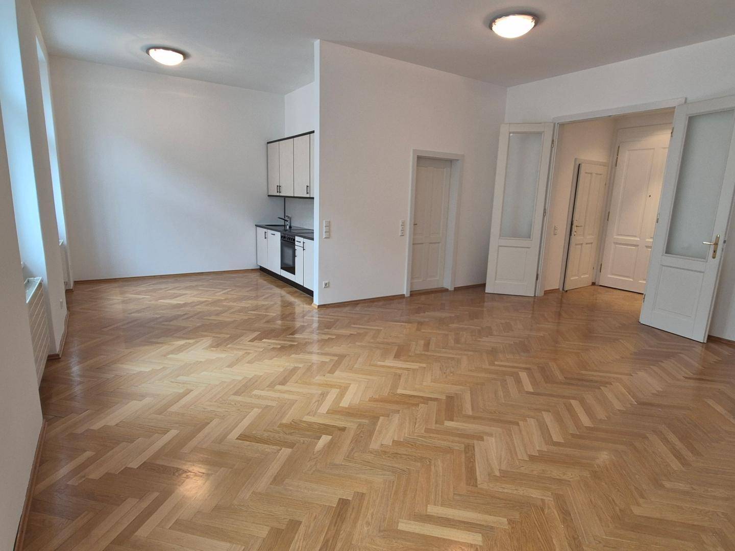 Geräumiger Wohnbereich mit Fischgrätparkett und integrierter Küchenzeile, ideal für offenes Wohnen.