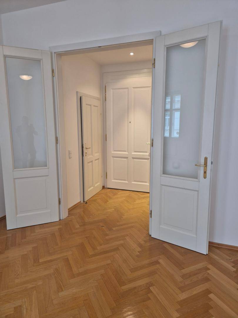 Heller Flur mit Fischgrätparkett und eleganten weißen Doppeltüren, die zu weiteren Räumen führen.