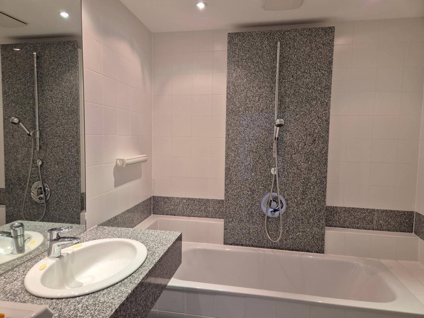 Modernes Badezimmer mit Badewanne, Einzelwaschbecken und grauen Granitfliesen.