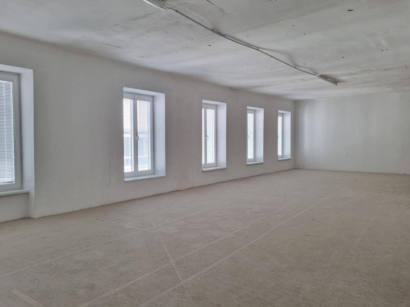 Großer, leerer Raum mit mehreren Fenstern und rohem Betonboden, bereit für den Ausbau.