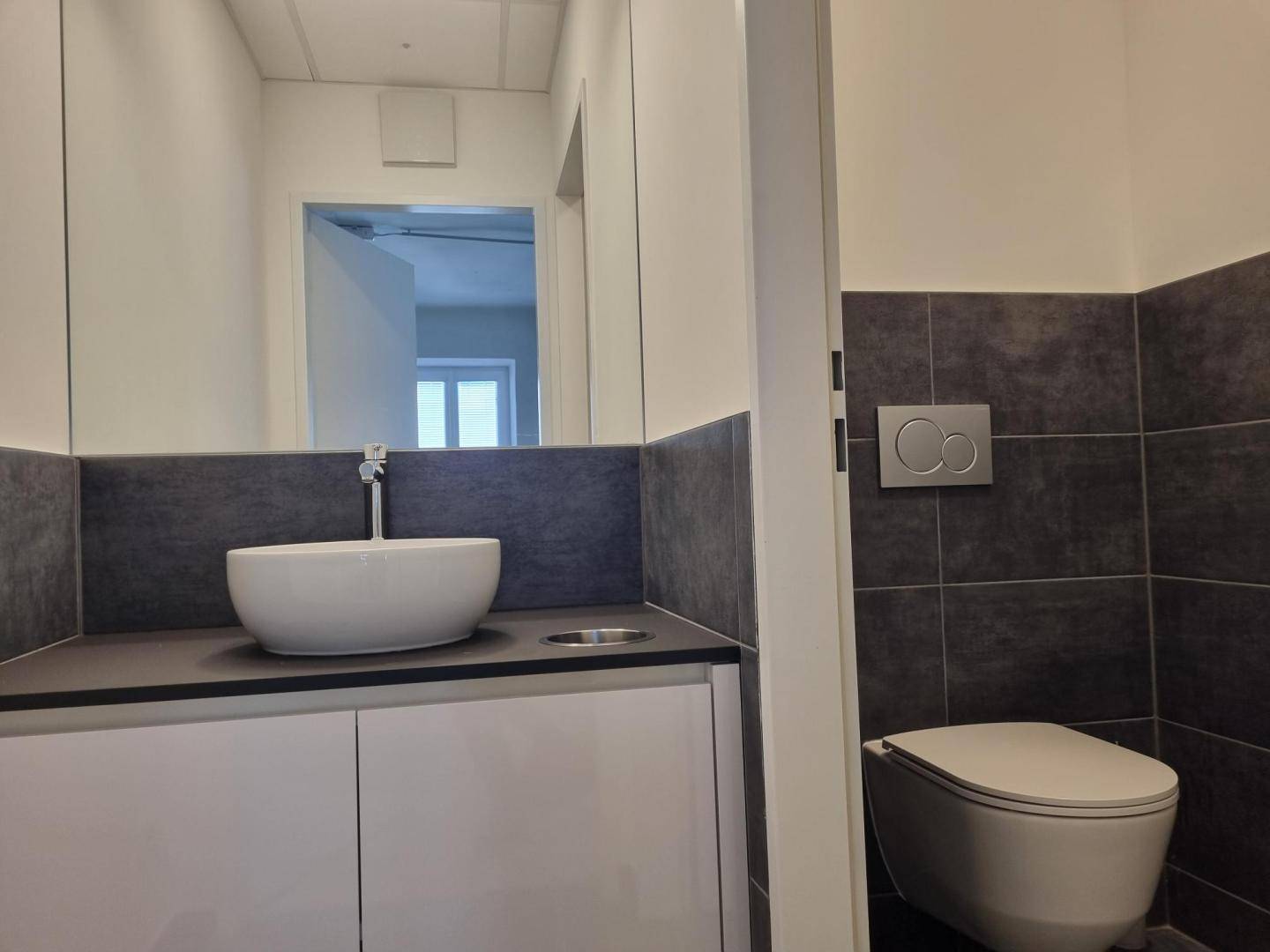 Modernes Badezimmer mit dunklen Fliesen, wandhängendem WC und einem Waschbecken auf einem Waschtisch.